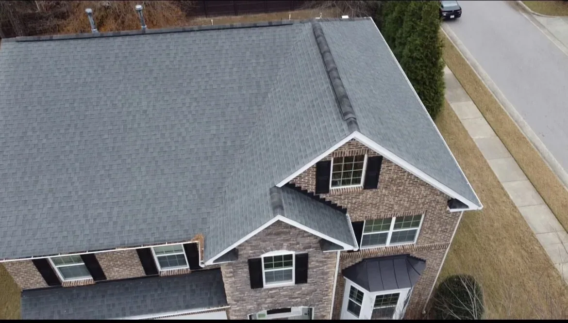 Drone view of a brick two-story home with a new roof and clean gutter line