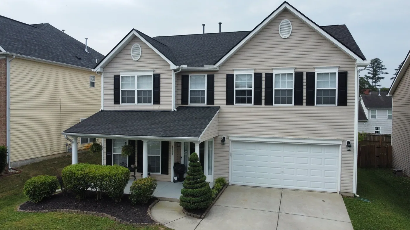Front elevation of a beige two-story home with black shutters and a new dark roof